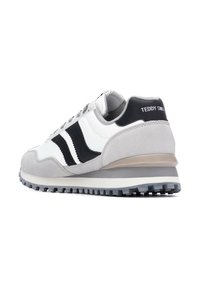 Zapatilla gris y blanca con acentos negros, materiales de gamuza y sintéticos, suela texturizada y logo en el talón. Diseño atlético clásico.