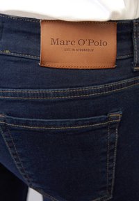 Donkerblauwe denim jeans met een leren taillebandpatch waarop "Marc O'Polo" en "EST. IN STOCKHOLM" in bruin is geperst.