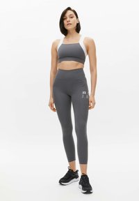 Grauer Sport-BH und hochtaillierte Leggings, beide aus einem glatten, dehnbaren Material. Schwarze Sportschuhe mit texturierten Details für besseren Halt.
