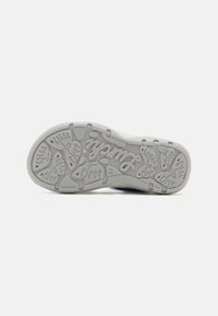 Puma sneakersåle, hovedsakelig hvit med en teksturert grå gummioverflate. Har mønstrede spor og "Puma"-logo i kursiv.