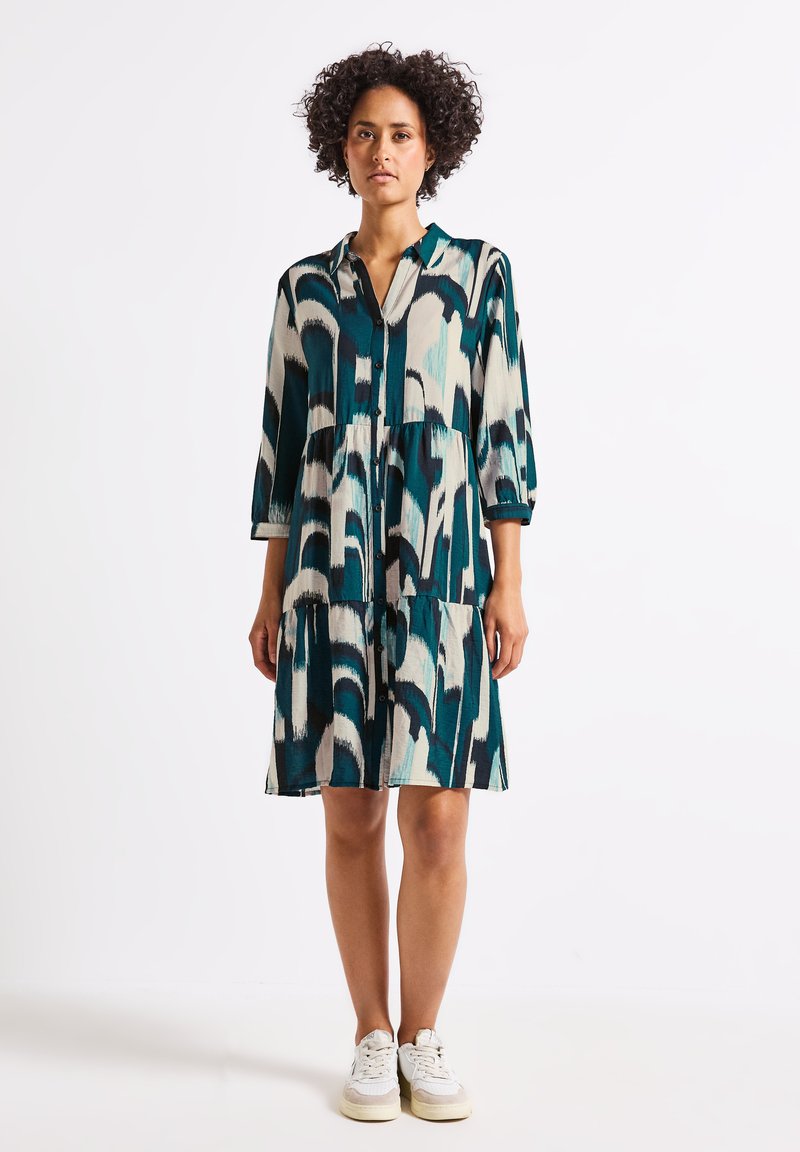 Vestito a camicia con un motivo astratto in tonalità di teal, nero e crema, maniche a tre quarti e design a strati. Texture del tessuto liscia.
