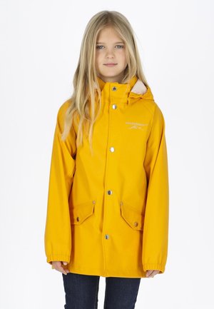 Jong meisje met lang blond haar, gekleed in een felgele regenjas met drukknoopsluiting en zakken aan de voorkant, staand tegen een witte achtergrond.