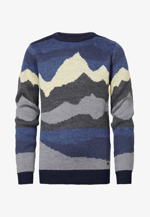 Pull en tricot avec motif de montagne en bleu, vert, gris et crème ; poignets et ourlet côtelés bleu marine. Associé à un jean gris clair et des baskets blanches.