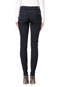 Jeans skinnies azul oscuro con una textura suave, cintura de altura media y costuras contrastantes sutiles en los bolsillos traseros. Combinando con tacones altos beige.