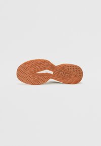 La semelle de la sneaker présente un caoutchouc marron texturé avec des motifs en zigzag et circulaires, conçue pour l'adhérence et la traction.