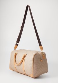 Μπεζ ταξιδιωτική τσάντα με γεωμετρικό σχέδιο, καφέ λεπτομέρειες, διπλές λαβές και ρυθμιζόμενο καφέ λουρί; λεία υφή και κλείσιμο με φερμουάρ.