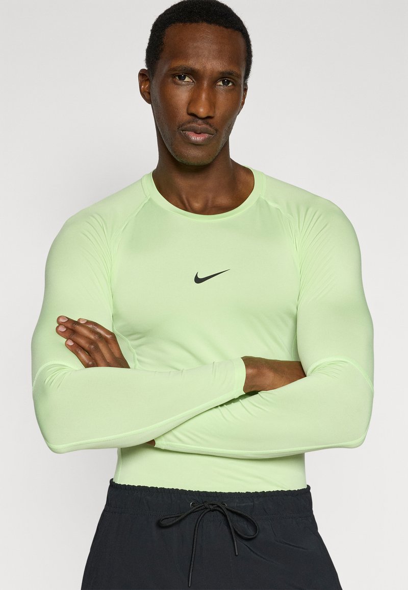 Langärmeliges Sportshirt in Hellgrün mit schwarzem Nike-Logo auf der Brust. Der Stoff wirkt glatt und das Design ist figurbetont.