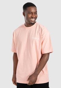 Lys pink bomulds T-shirt med korte ærmer og rund hals, med hvid "SMILODOX Ltd." logo på venstre bryst.