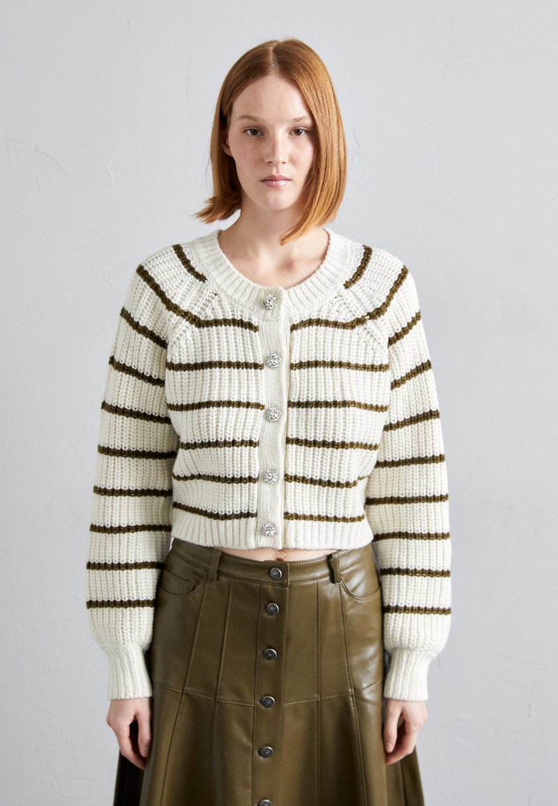 Hvit strikket cardigan med brune striper, med ribbestrikket krage og mansjetter, og fem dekorative knapper foran.
