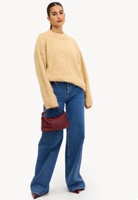Un pull en laine beige et moelleux, un jeans bleu à jambes larges et un petit sac en osier bordeaux. Design minimaliste avec des manches longues et une coupe décontractée.
