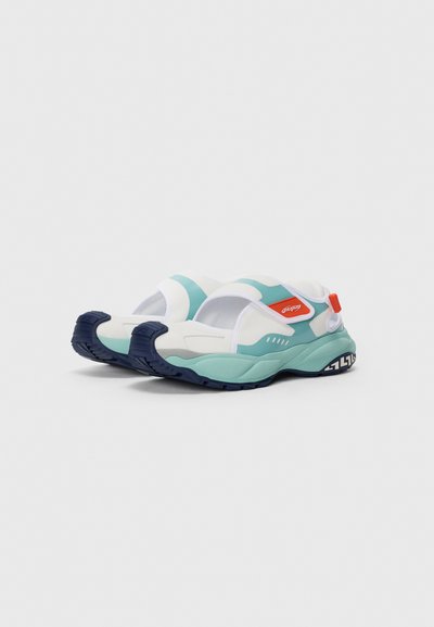 Vita och teal slip-on sneakers med marinblå sulor, orange dragrem och rundad tådesign, visad från en framsida vinkel mot vit bakgrund.