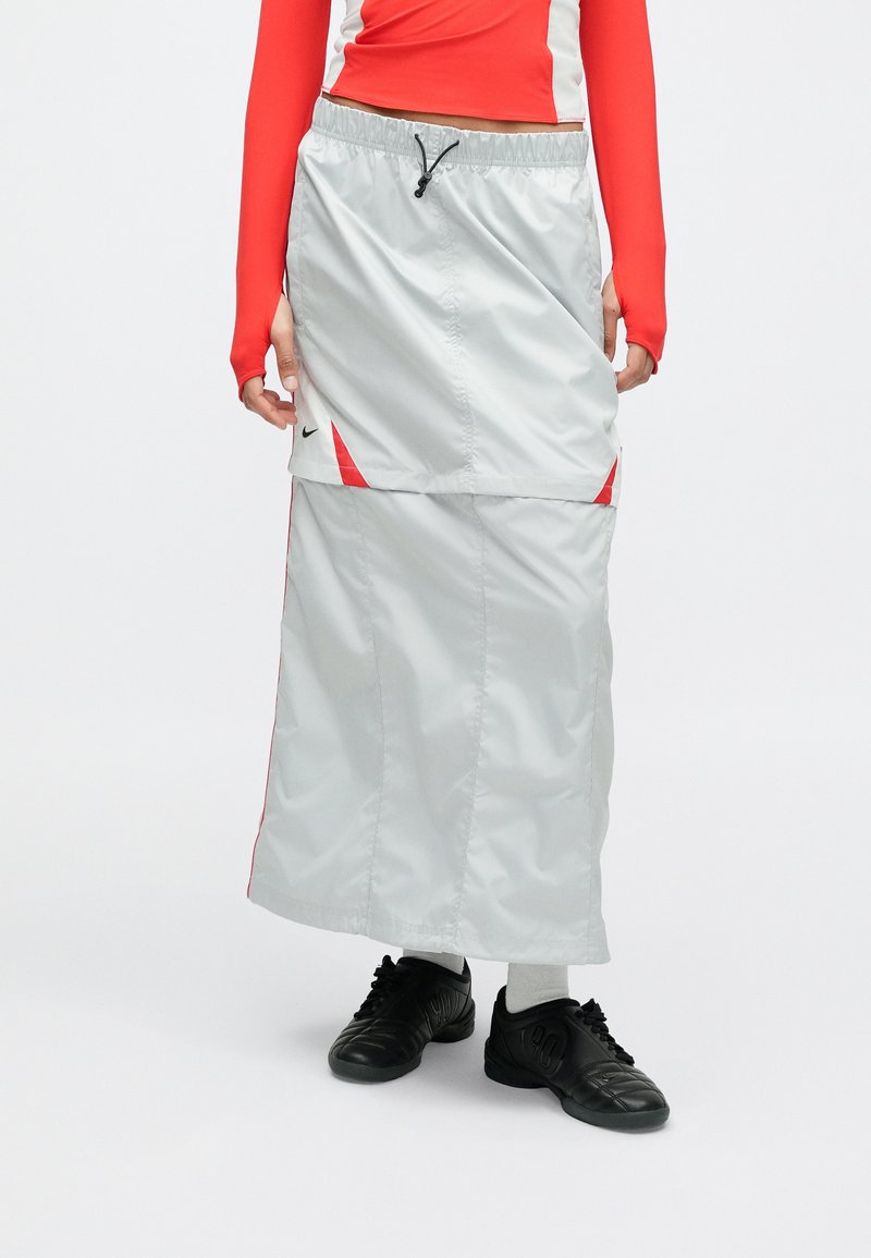 Lichtgrijze, lange sportrok met rode accenten, gemaakt van lichtgewicht materiaal. Elastische tailleband met trekkoord, zijslit-details.