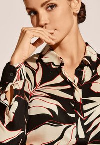 Black blouse featuring a floral pattern in cream and red; classic collar, buttoned cuffs, and smooth texture. Close-up view.