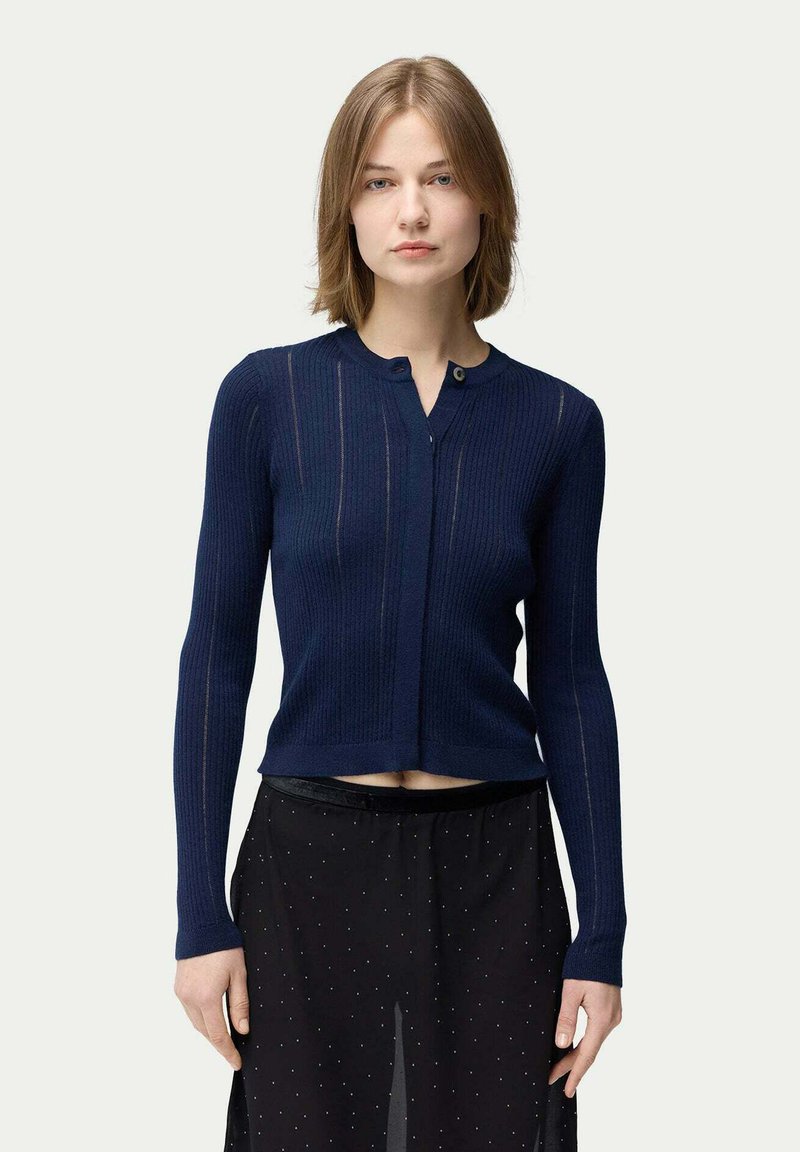 Marinblå ribbstickad kofta med kort längd, långa ärmar och knäppning. Texturerad tyg med vertikala linjer och en figurnära design.