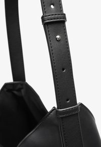 Cinghia regolabile in pelle nera con fibbia argentata e multiple forature per la personalizzazione della taglia, attaccata a una borsa nera.