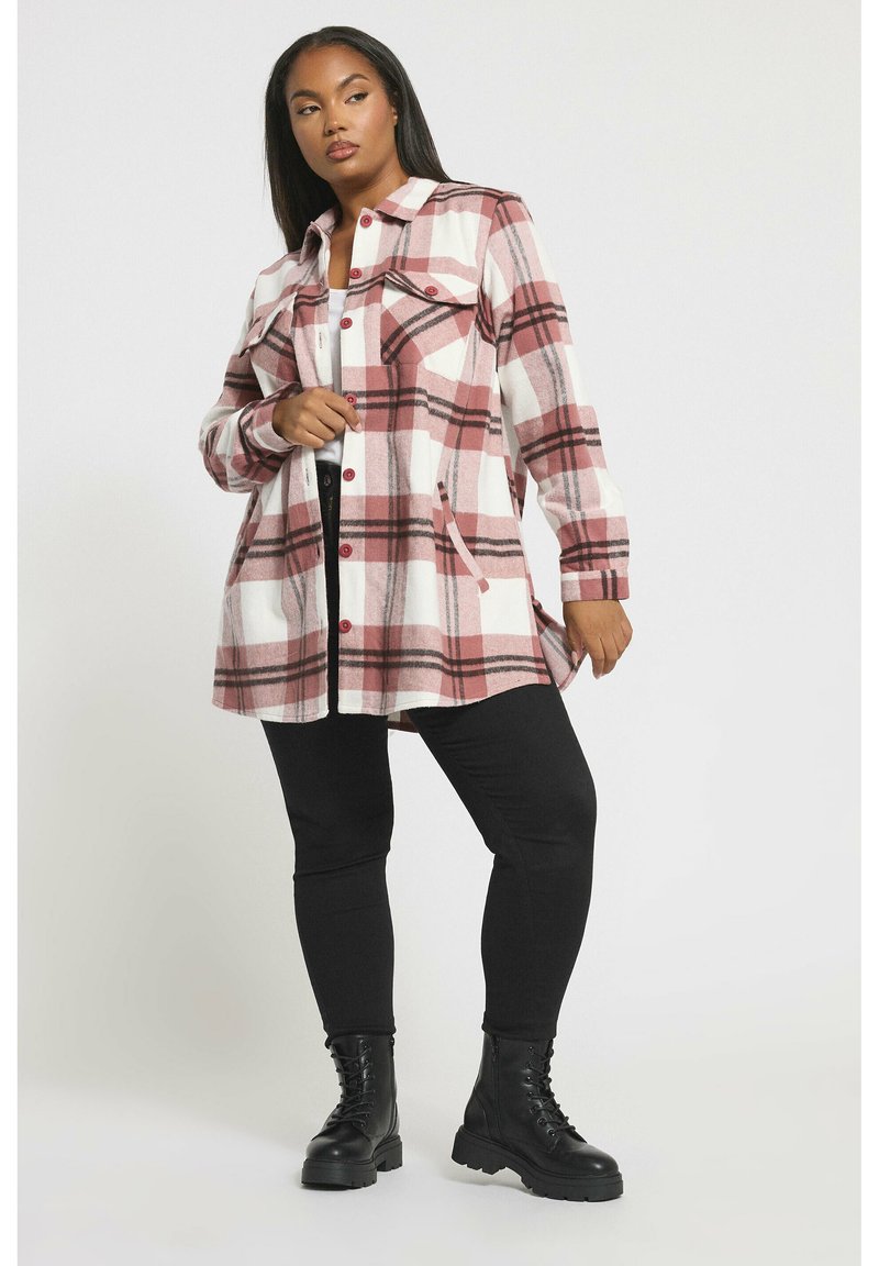 Czerwona i biała koszulowa kurtka z kieszeniami, kołnierzem i frontowymi guzikami, w połączeniu z czarnymi legginsami i masywnymi czarnymi botkami.