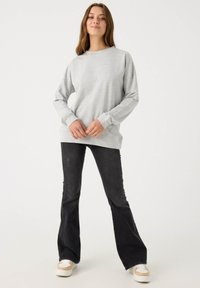 Sudadera de manga larga gris claro con cuello redondo, combinada con jeans acampanados negros. Las zapatillas cuentan con acentos en blanco y marrón claro.