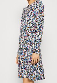 Kwiatowa sukienka z niebieskimi, białymi i pomarańczowymi wzorami na ciemnym tle, z długimi rękawami, luźnym krojem i zaokrąglonym dekoltem.