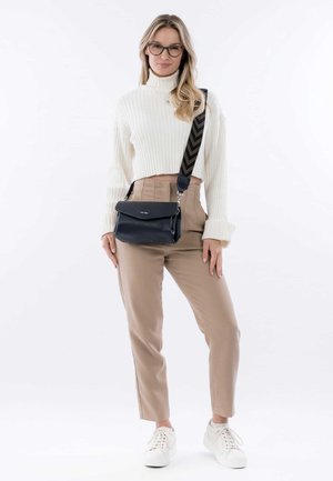 Zwarte crossbody tas van textuurmateriaal, met klepsluiting en een patroonriem. Draagt bij beige hoge taillebroek en een witte geribbelde trui.