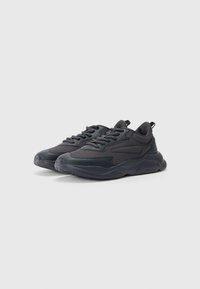 Black sneakers feature a mix of smooth and textured materials, a raised sole, and a supportive tongue with lace-up design and pull tab.
