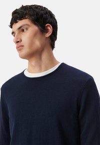 Granatowy sweter z okrągłym białym kołnierzykiem, wykonany z miękkiego materiału. Design charakteryzuje się prostą, klasyczną sylwetką z teksturowanym wykończeniem.