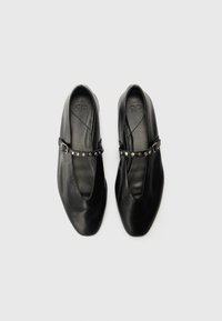 Čierne kožené ploché topánky s špicatou špičkou, vybavené úzkym členkovým pásikom ozdobeným malými kovovými hrotmi. Hladký povrch po celom obvode.