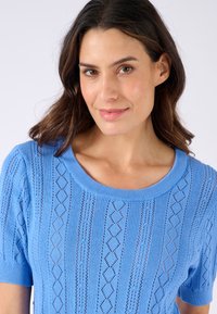 Suéter de manga corta en azul claro que presenta un cuello redondo acanalado y un patrón de punto de encaje en forma de diamante con detalles en horizontal y vertical.