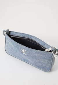 Sac en denim avec quincaillerie en argent, fermeture zippée et logo. Présente une forme rectangulaire et un tissu texturé. L'intérieur est doublé en noir.