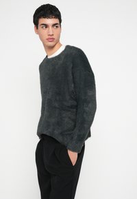 Tmavomodrý huňatý sveter s okrúhlym výstrihom a dlhými rukávmi, nosený cez čierne nohavice. Viditeľná mäkká textúra. Jednoduchý, uvoľnený dizajn.