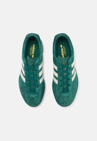 Gröna mockaskor för sport med vita läderränder, snörningsdesign och en texturerad sula. Guldlogotypdetaljer på tungan och innersulan.