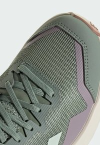  chaussure de sport verte avec une tige en maille texturée, des accents synthétiques en lavande et beige clair, et des lacets plats. Présente un embout renforcé.