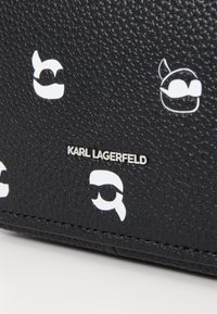 Black textured leather bag featuring white graphic logos and a metallic "KARL LAGERFELD" inscription. Compact and modern design.
