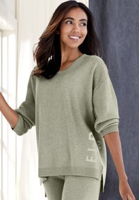 Hellgrüner, gestrickter Pullover mit rundem Halsausschnitt, gerippten Bündchen, seitlichen Schlitzen und Textdetail auf der Vorderseite, kombiniert mit passenden Hosen.