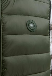 Zielona oliwkowa kamizelka ocieplana z okrągłą naszywką z logo "JACK & JONES". Gładka tekstura materiału i stębnowane poziome panele.