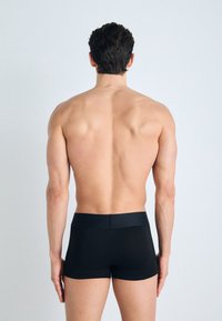 Boxer shorts noirs avec une texture lisse et une taille élastique, vus de l'arrière sur un modèle sans vêtement sur le haut du corps.
