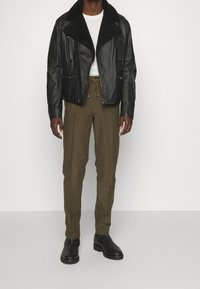 Svart läderjacka med en shearlingkrage; två fickor med dragkedja och två sidfickor. Olivgröna byxor och svarta läderstövlar fulländar outfiten.