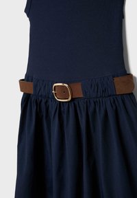 Marineblå kjole med ribbet top og samlet nederdel, indsnævret i taljen med et brunt ruskindsbælte med en guldfirkantet spænde.