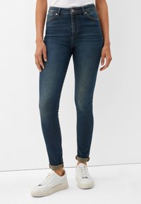 Vaqueros de tiro alto azul oscuro con un corte ajustado, que presentan un ligero desgaste y puños arremangados, combinados con zapatillas blancas para un look casual.