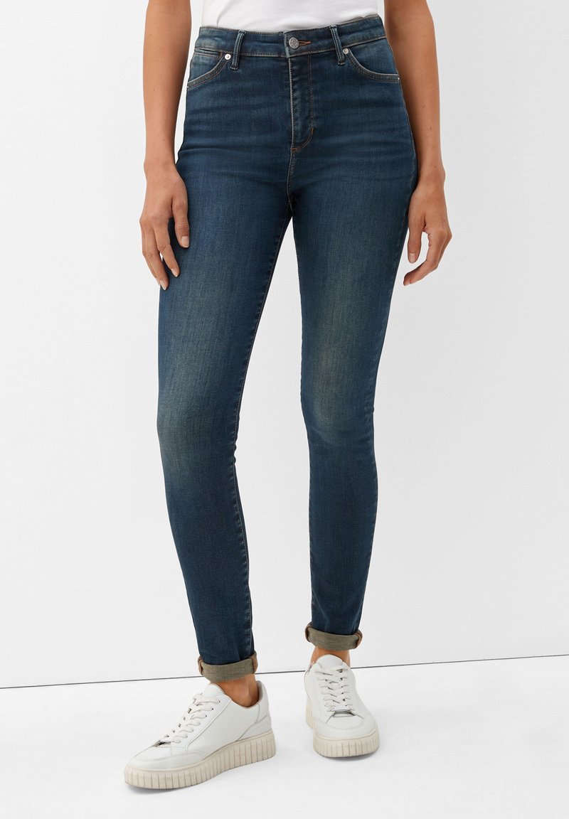 Vaqueros de tiro alto azul oscuro con un corte ajustado, que presentan un ligero desgaste y puños arremangados, combinados con zapatillas blancas para un look casual.