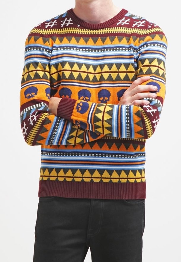 Gestrickter Pullover mit mehrfarbigen, tribal-inspirierten Mustern, bordeauxrotem Rand, Totenkopfmotiven und Streifen in Orange, Blau, Gelb und Schwarz.