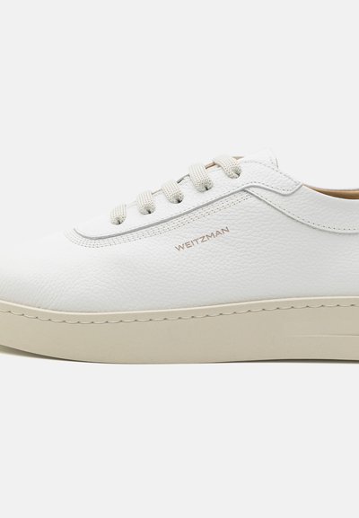 Zapatilla blanca de piel con parte superior texturizada, punta redonda y suela de goma beige. Presenta cordones de color beige claro y el nombre de la marca en relieve en el lateral.