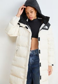 Zachte, lange parka in gebroken wit met een zwarte capuchon, voorzien van een ritssluiting en zijzakken, gemaakt van glad, geïsoleerd materiaal.