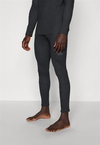 Top termico nero a maniche lunghe con leggings aderenti abbinati. Entrambi i capi hanno una texture liscia e presentano un branding discreto sulla gamba.