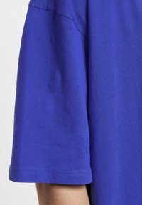 Korte mouwen T-shirt van helderblauwe stof. Glad oppervlak met een ronde hals en gestikte zoom. Heeft een ontspannen pasvorm en standaard mouwlengte.