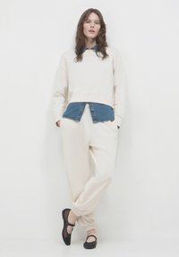Felpa accorciata color crema sovrapposta a una camicia di jeans, abbinata a pantaloni larghi color crema e ballerine nere con polsini elasticizzati.