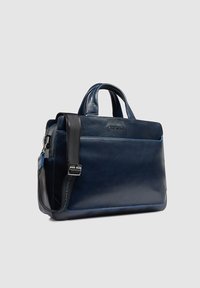 Bolso de cuero azul marino con dos asas y una correa desmontable. Cuenta con un bolsillo frontal, costuras azules y una elegante forma rectangular.