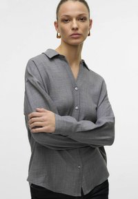 Gray button-up shirt with a collar, long sleeves, and a relaxed fit. The fabric has a subtle texture, featuring light buttons and a curved hem.