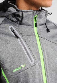 Veste de sport grise avec un col haut, doté d'une fermeture éclair néon verte et d'accents, en tissu texturé, et avec une poche poitrine zippée.