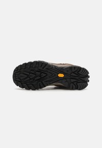 Trail schoenen met een robuuste zwarte rubberen zool met een diep profiel. Lichtbruine bovenkant met textuuraccenten en merkdetails.