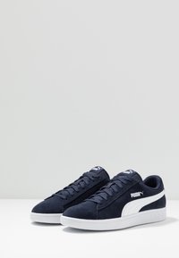 Navy suede sneakers with white rubber sole, featuring a textured upper, flat laces, and prominent PUMA logo on the side and tongue.